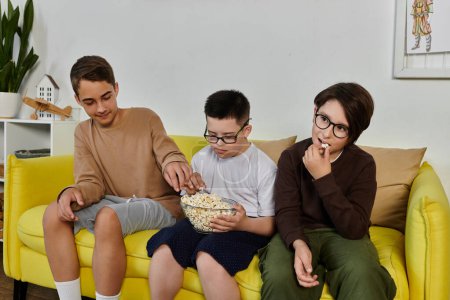 Three boys relax on a yellow couch, sharing popcorn and enjoying each others company.