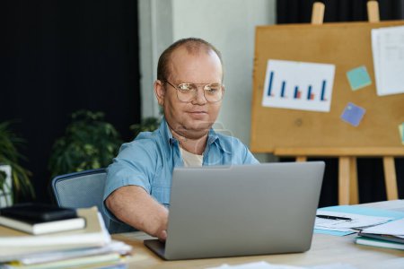 Ein inklusiver Mann sitzt an seinem Schreibtisch, konzentriert auf seine Arbeit am Laptop..