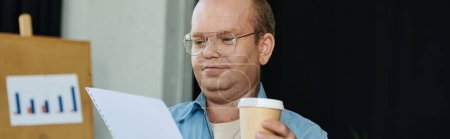 A man with inclusivity wearing glasses carefully examines documents while holding a cup of coffee.