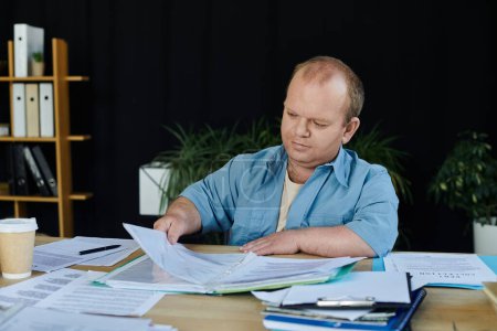Ein inklusiver Mann sitzt an einem Schreibtisch und sichtet fleißig Papiere.