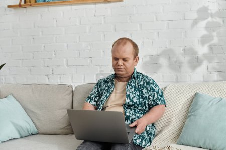 A man with inclusivity sits on a couch using a laptop.
