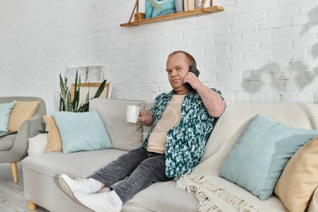 A man with inclusivity relaxes on a couch, enjoying a cup of coffee and a phone call in his comfortable home.