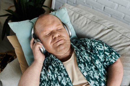 Un homme inclusif est allongé sur un canapé, portant un casque, les yeux fermés, écoutant de la musique.