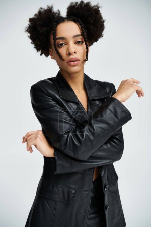 A stylish young African American woman poses in a black leather jacket against a grey background.