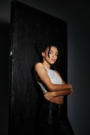 A stylish young African American woman in a white tank top poses confidently against a dark grey background, showcasing fashion and trends.