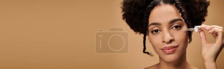 Eine junge afroamerikanische Frau trägt Serum auf ihr Gesicht auf, während sie in die Kamera blickt.