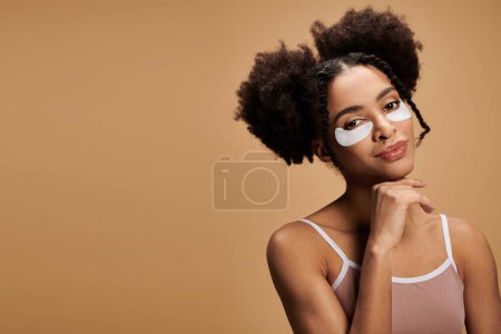 Photo for A young woman with dark curly hair and eye patches smiles confidently against a warm beige backdrop. - Royalty Free Image