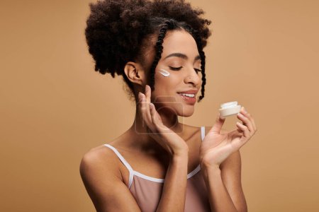 Photo for A young African American woman applies cream to her face, enjoying a moment of self-care. - Royalty Free Image