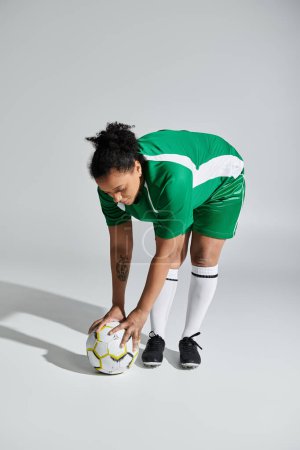 A woman in a green jersey bends down to the ground, preparing for a play during a football match.