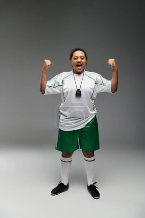 Una atlética con uniforme de fútbol celebra una victoria con una pose triunfante.