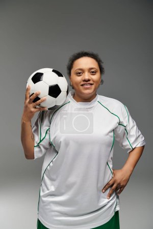 Una mujer en un jersey blanco sostiene una pelota de fútbol y sonríe a la cámara.