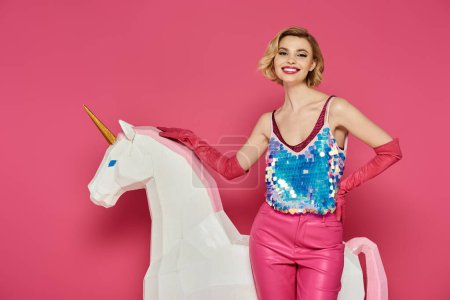 Woman on white unicorn smiles in pink outfit on pink background.