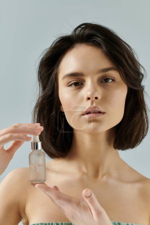 Dark-haired woman holds glass bottle with dropper, gazing at viewer.