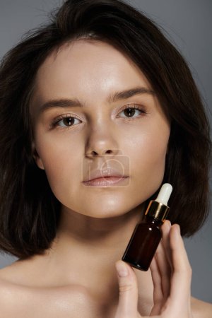 Photo for A close-up portrait of a woman holding a small bottle of serum, her gaze captivating. - Royalty Free Image