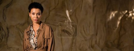 morena arqueólogo en chaqueta marrón mirando a la cámara en la cueva, pancarta