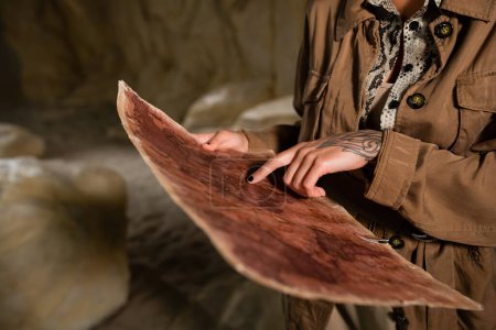 Ausgeschnittene Ansicht eines Archäologen in brauner Jacke, der auf eine antike Landkarte in der Höhle zeigt