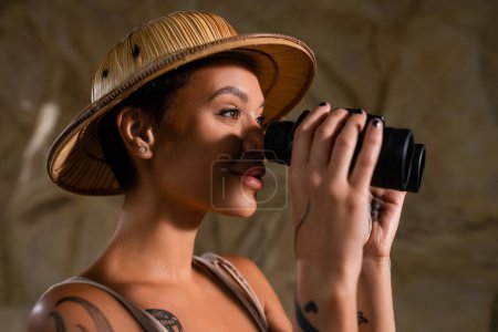 young archaeologist in safari hat looking through binoculars in desert