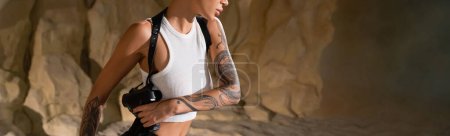 partial view of tattooed archaeologist with gun in holster, banner