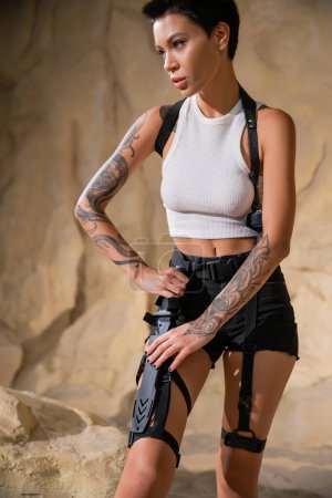 tattooed and sexy archaeologist with short hair taking sharp knife from holster
