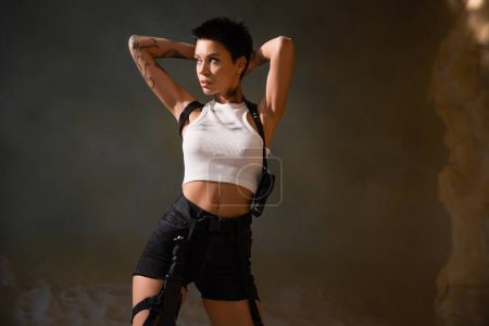 sexy and armed archaeologist with tattoo and dirty crop top looking away