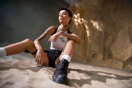 low angle view of young archaeologist with tattoo and short hair sitting in sexy outfit 