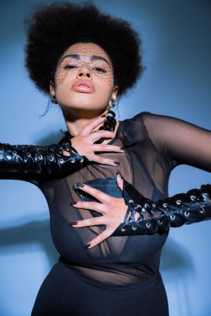 stylish african american woman with laced-up leather sleeves posing on blue