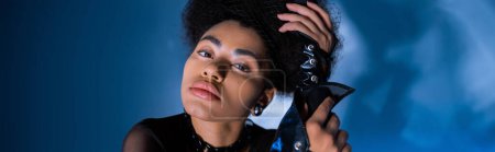 stylish african american woman in lace-up leather sleeves posing on blue, banner