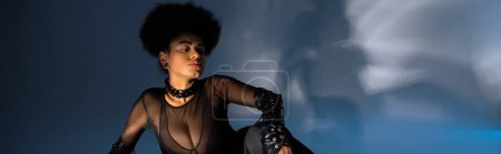Téléchargez les photos : Femme afro-américaine bouclée en chemise transparente et tenue sexy assise sur bleu, bannière - en image libre de droit