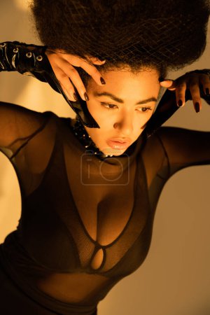 trendy african american model in transparent shirt and black bra posing on yellow 