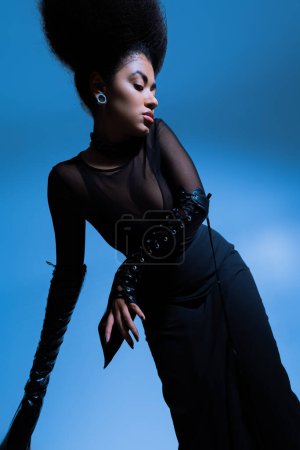 curly african american model in black outfit posing while looking away on blue
