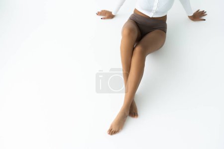 high angle view of cropped young african american woman in long sleeve shirt and panties sitting on white 