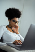 concentrated african american woman in eyeglasses using laptop at home Poster #618994330