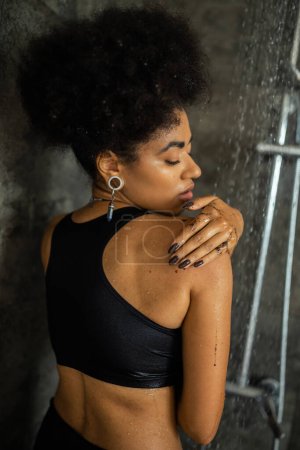 Téléchargez les photos : Jeune femme afro-américaine appliquant un gommage au café sur l'épaule près de l'eau trouble dans la douche - en image libre de droit