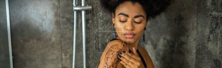 Mujer afroamericana joven masajeando cuerpo con exfoliante en cabina de ducha, pancarta 