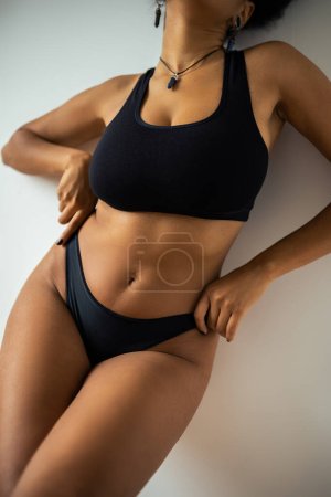 Cropped view of young african american woman in crop top touching black panties near wall 