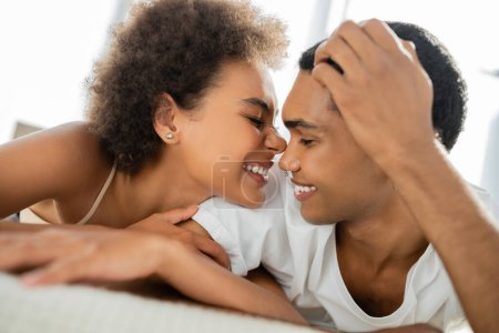 fröhliche afrikanisch-amerikanische Frau grimmig neben lächelndem Freund auf dem Bett