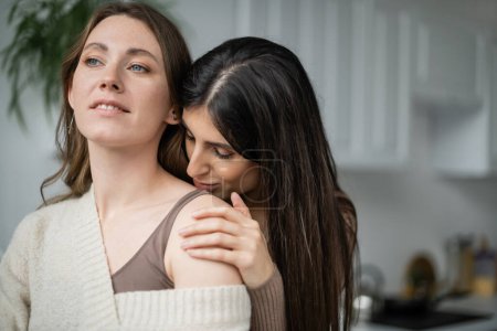 Mujer joven besándose hombro de pareja lesbiana en cocina 