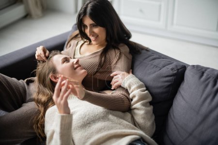 Photo for Smiling lesbian woman touching hand of girlfriend on couch at home - Royalty Free Image