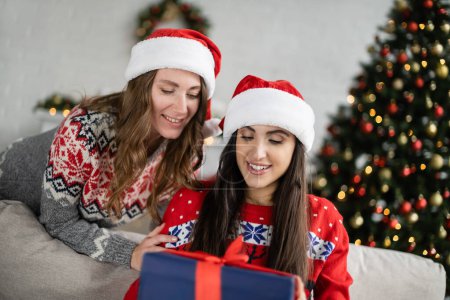 Positives lesbisches Paar in Weihnachtsgeschenken sieht verschwommenes Neujahrsgeschenk zu Hause 