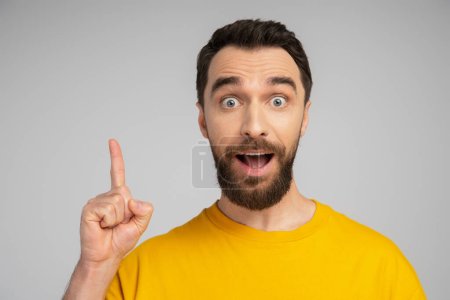 astonished brunette man showing idea sign and looking at camera isolated on grey