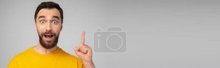 Foto de Hombre barbudo excitado mostrando gesto de idea mientras mira la cámara aislada en gris, pancarta - Imagen libre de derechos