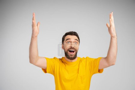 Téléchargez les photos : Homme étonné en t-shirt jaune debout avec la bouche ouverte et montrant wow geste isolé sur gris - en image libre de droit