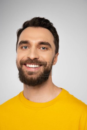 Porträt eines fröhlichen brünetten Mannes mit Bart, der isoliert auf grau in die Kamera blickt