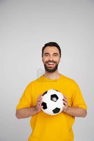 Foto de Alegre barbudo fanático de los deportes con pelota de fútbol mirando a la cámara aislado en gris - Imagen libre de derechos