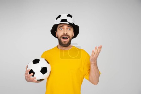 Foto de Sorprendido y molesto ventilador de fútbol apuntando con la mano mientras mira hacia otro lado aislado en gris - Imagen libre de derechos