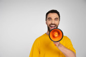 excited man screaming in megaphone and looking at camera isolated on grey mug #621217312