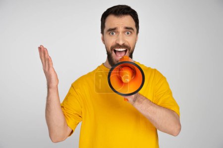 Photo for Displeased man in yellow t-shirt shouting in loudspeaker isolated on grey - Royalty Free Image