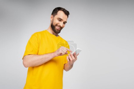 low angle view of brunette bearded man pointing at mobile phone isolated on grey
