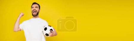 shouting football fan with ball rejoicing and showing triumph gesture isolated on yellow, banner