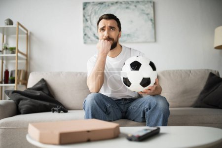 Foto de KYIV, UCRANIA - 21 de octubre de 2022: hombre preocupado sosteniendo el fútbol y viendo el campeonato en casa - Imagen libre de derechos